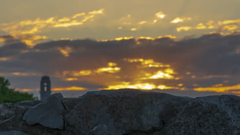 Eleganter-Sonnenaufgang-Im-Zeitraffer-Mit-Sonne,-Die-über-Einer-Vordergrundwand-Emporsteigt,-Mit-Lichtstrahlen-Durch-Die-Wolken