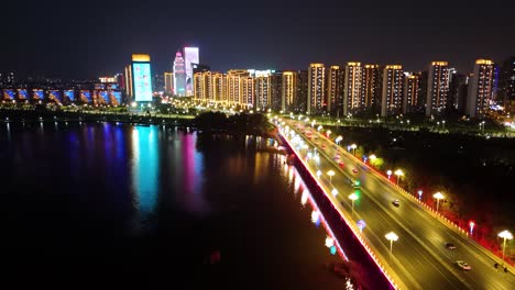 Nighttime-aerial-view-of-illuminated-buildings-near-the-riverside-in-Linyi-City,-Shandong-Province