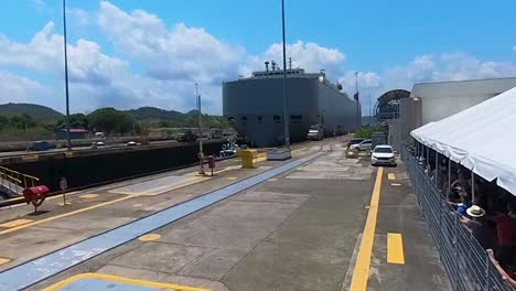 Vista-De-Un-Barco-En-Tránsito-Por-El-Canal-De-Panamá-Y-Espectadores-En-El-Centro-De-Visitantes-De-Miraflores.