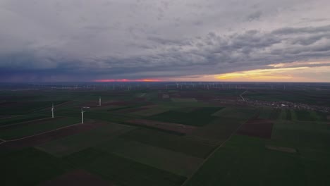 Wind-farm-on-green-fields-under-dramatic-stormy-sky-at-sunset