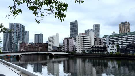 Moderne-Skyline-Einer-Stadt-Mit-Hohen-Gebäuden,-Die-Sich-An-Einem-Bewölkten-Tag-In-Einem-Ruhigen-Fluss-Spiegeln