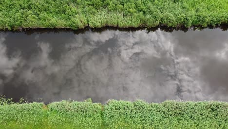 Aerial-view-of-a-calm-river-with-the-sky's-reflection,-framed-by-lush-green-vegetation