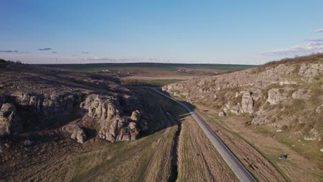 Scenic-aerial-view-of-Dobrogea-gorges-with-winding-road-and-rugged-landscape-under-clear-blue-sky