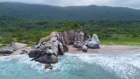 Scenic-Beach-with-Turquoise-Waters,-Beach-and-Large-Smooth-Boulders-with-Green-Forest-in-the-Background,-Aerial-Drone-Shot