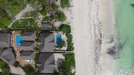 Aerial-drone-tops-down-pristine-turquoise-sea-water-white-sand-beach-at-Pingwe-Zanzibar-zooming-into-waterfront-resorts