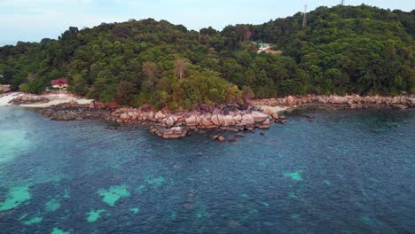 Capturing-the-beauty-of-a-tropical-island,-turquoise-waters-and-rocky-coastline,-this-aerial-view-shows-vibrant-blue-and-green-hues-against-rugged-cliffs-and-shores