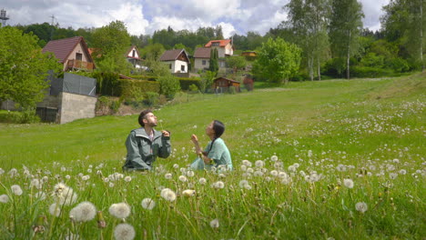 Glückliches-Paar-Sitzt-Auf-Einer-Frühlingswiese-Und-Bläst-Löwenzahnblüten-In-Der-Nähe-Des-Dorfes-Cesky-Krumlov-In-Der-Tschechischen-Republik