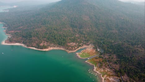 Aerial-Drone-Flyover-Lake-Shore,-Hazy-Foothill-Forests,-Campgrounds-And-Cabins-At-Bass-Lake,-California