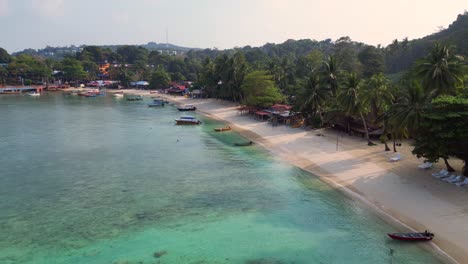 Morning-mood-Aerial-view-speed-ramp-of-a-tropical-island-with-a-long-wooden-pier-leading-to-a-floating-restaurant,-surrounded-by-turquoise-waters-and-lush-green-rainforest