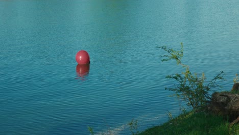 Una-Sola-Boya-Roja-Flotando-En-Las-Tranquilas-Aguas-Azules-Del-Lago-Jarun-En-Zagreb,-Croacia.