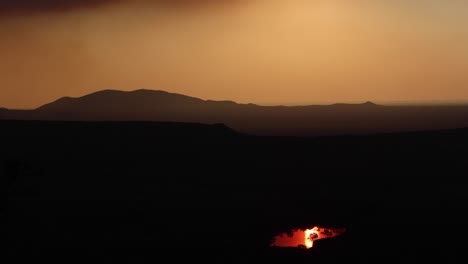 Dramatischer-Orange-roter-Afrikanischer-Sonnenuntergang-Unter-Rauchwolken-Mit-Einem-Damm,-Der-Die-Sonne-Aus-Dem-Dunklen-Vordergrund-Wie-Ein-Topf-Voll-Gold-Reflektiert