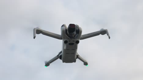 Low-angle-looking-up-at-hovering-isolated-DJI-Mini-4-Pro-drone-against-cloudy-sky