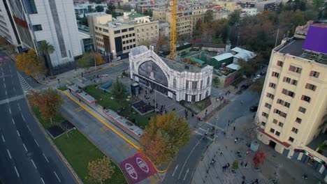 Aerial-Establishing-above-Pirque-station-street-landmark-of-Santiago-de-Chile,-streets-and-pedestrians-during-autumn-daylight,-drone-shot