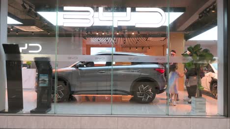 Car-dealership-from-the-Chinese-Electric-Vehicle-car-company-BYD,-customers-explore-vehicles-while-pedestrians-navigate-the-bustling-street