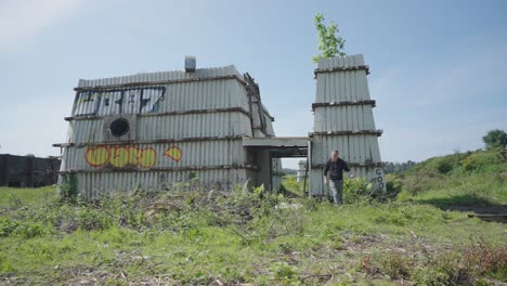 Man-searching-unusual-abandoned-construction,-derelict-exterior,-slow-mo