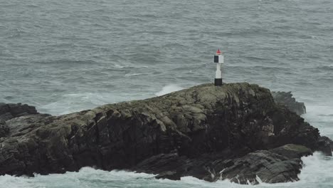 Small-beacon-on-coastal-rock-during-stormy-weather,-static-view