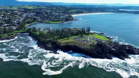 Landscape-stunning-view-of-Kiama-blowhole-and-lighthouse-carpark-main-suburb-town-harbour-coastline-rocky-headland-sea-ocean-South-Coast-tourism-travel-drone-aerial