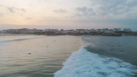 Drone-Siguiendo-Grandes-Olas-Barriendo-La-Puesta-De-Sol-De-Los-Surfistas-En-Peniche,-Portugal