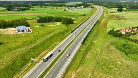 Luftaufnahme-Einer-Autobahn,-Die-Durch-Eine-Ländliche-Landschaft-Mit-Umliegenden-Grünen-Feldern-Und-Verstreuten-Häusern-Verläuft