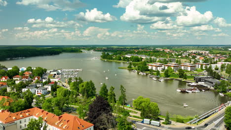 Aerial-view-of-a-lakeside-Iława-with-red-roofed-buildings,-marinas,-and-boats-on-the-water