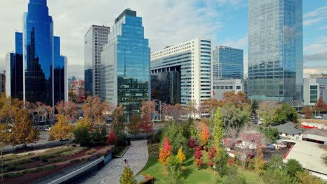 AERIAL:-rising-in-front-of-fall-colors-in-the-Titanium-park-of-Las-Condes,-Chile