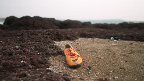 Orange-shoe-on-a-rocky-beach,-abandoned-and-weathered