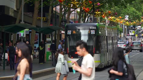 Straßenszene-Im-Zentralen-Geschäftsviertel-Von-Melbourne-Mit-Straßenbahnen,-Fußgängern-Und-Festlichen-Dekorationen,-Die-Das-Pulsierende-Stadtleben-Widerspiegeln,-Zeitlupenaufnahme,-Die-Das-Geschäftige-Treiben-Der-Stadt-Einfängt