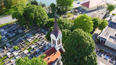 Aerial-Descent-Over-Szent-Kereszt-Cemetery-Cathedral-with-Spiraling-Drone-View-of-the-Spire,-Graveyard,-and-Lush-Surroundings-in-Kapuvár,-Hungary