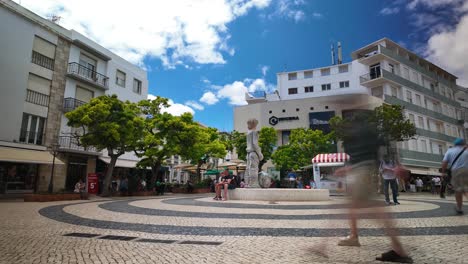 Timelapse-of-people-walking-in-a-vibrant-square-in-Lagos,-Portugal,-with-colorful-shops-and-trees