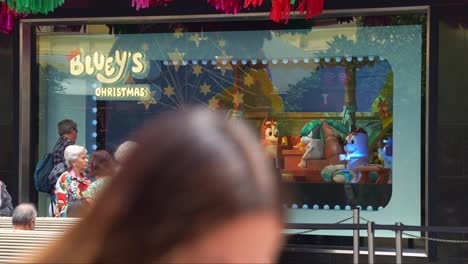 People-lineup-for-the-famous-Bluey's-Christmas-display-in-the-Myer's-windows-in-bustling-downtown-Melbourne-City,-Bourke-Street-Mall-during-Christmas-season,-with-pedestrians-passing-by-in-the-scene