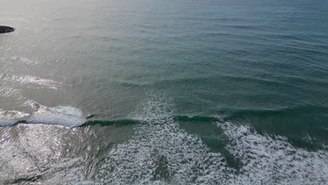 The-rocky-coastline-and-ocean-waves-at-the-port-of-ginesta-in-barcelona,-aerial-view