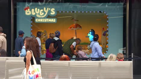 Crowds-lineup-for-the-famous-Bluey's-Christmas-display-in-the-Myer's-windows-in-bustling-downtown-Melbourne-City,-Bourke-Street-Mall-during-Christmas-season,-with-pedestrians-passing-by-in-the-scene