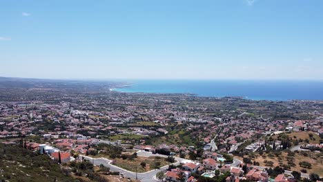 Panoramic-aerial-view-of-Peyia,-Cyprus,-with-sprawling-town,-lush-fields,-and-the-Mediterranean-Sea-under-a-clear-blue-sky