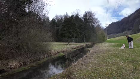 Blick-Auf-Einen-Kanal-Mit-Einer-Frau-Und-Ihrem-Hund,-Die-Tagsüber-Spielen