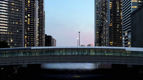 A-pedestrian-bridge-illuminated-at-dusk-between-tall-buildings-in-a-cityscape