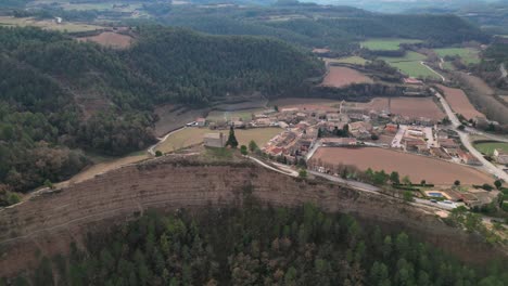 The-old-town-of-oristà-nestled-in-a-scenic-valley-surrounded-by-lush-forests-and-hills,-aerial-view