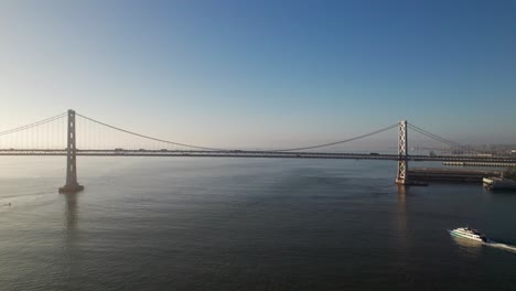 Wunderschöne-Neblige-Luftaufnahme-Der-San-Francisco-Oakland-Bay-Bridge-Mit-Fähre-Im-Vordergrund,-4k