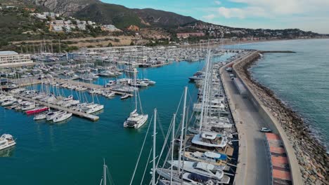 Port-ginesta-marina-with-sailboats-in-a-serene-coastal-setting-near-barcelona,-aerial-view