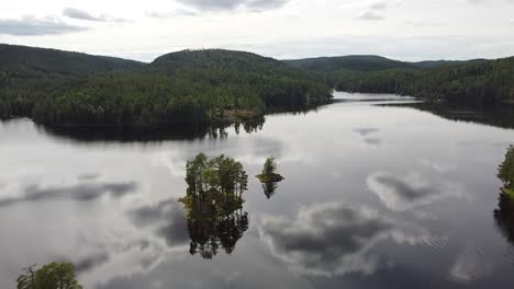 A-peaceful-lake-in-Norway-surrounded-by-lush-green-forests,-with-small-tree-covered-islands-reflecting-on-the-calm-water