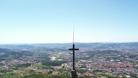 Aerial-view-of-Monte-da-Penha-church-cross-overlooking-Guimarães,-Portugal,-under-a-clear-blue-sky