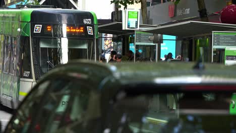 The-tram-arrives-at-the-Collins-Street-and-Swanston-Street-tram-stop,-where-passengers-wait-to-board,-slow-motion-shot-captures-the-vibrant-Melbourne-urban-lifestyle