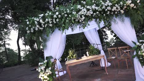 Un-Altar-De-Bodas-Al-Aire-Libre-Bellamente-Decorado,-Adornado-Con-Flores-Blancas-Y-Vegetación,-Luz-Del-Atardecer