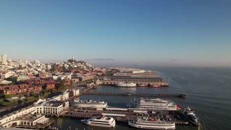 Muelles-Y-Barcos-En-Los-Muelles-De-San-Francisco-Con-La-Icónica-Torre-Coit,-Toma-Aérea-Frente-Al-Mar-De-4k