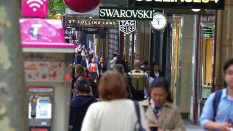 En-La-Bulliciosa-Ciudad-Del-Centro-De-Melbourne,-Una-Toma-En-Cámara-Lenta-Captura-A-Las-Grandes-Multitudes-Caminando-Por-Collins-Street,-Llena-De-Tiendas-Y-Boutiques-De-Lujo.