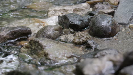 Agua-Suavemente-Ondulada-En-Un-Arroyo-De-Montaña-Con-Piedras-Oscuras