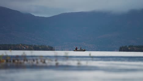 Two-people-paddle-across-the-fjord-in-a-small-rowing-boat,-with-forest-covered-rocky-shores-serving-as-a-picturesque-backdrop