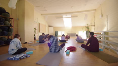 Seated-yogis-in-group-yoga-class-rock-bodies-from-side-to-side,-rear-shot