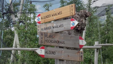 Wooden-hiking-trail-signs-in-front-of-apple-trees-on-the-irrigation-channel-trail-of-Algund---Lagundo,-South-Tyrol,-Italy