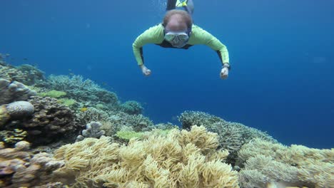 Swimming-over-a-colorful-coral-reef,-a-snorkeler-extends-his-arms,-immersed-in-the-marine-beauty