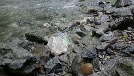 Water-gurgling-in-a-mountain-stream,-with-rocks-and-a-pebbly-shore